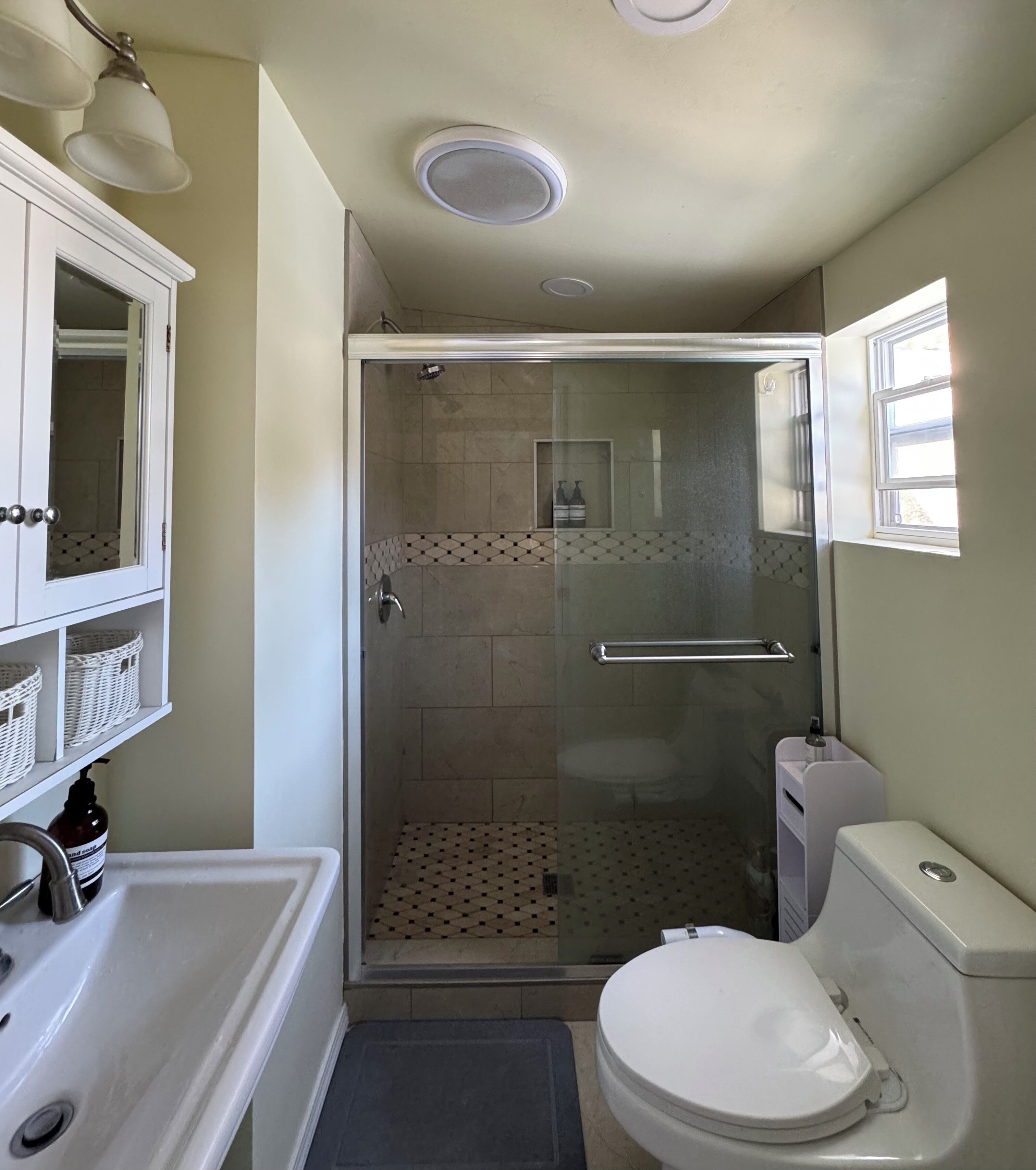 A bathroom with a glass-enclosed shower, a toilet, a sink, and a mirror.