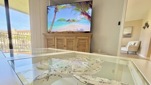 Una sala de estar moderna con una mesa de centro de vidrio, un televisor de pantalla plana en la pared y vistas a un balcón con mobiliario exterior.