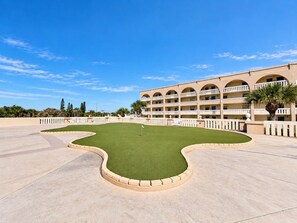 Un patio de hotel con un césped central, piscina y un edificio de varios pisos con balcones.
