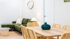 Ett rum med ett matbord, stolar, en grön soffa, en lampa och en vas.