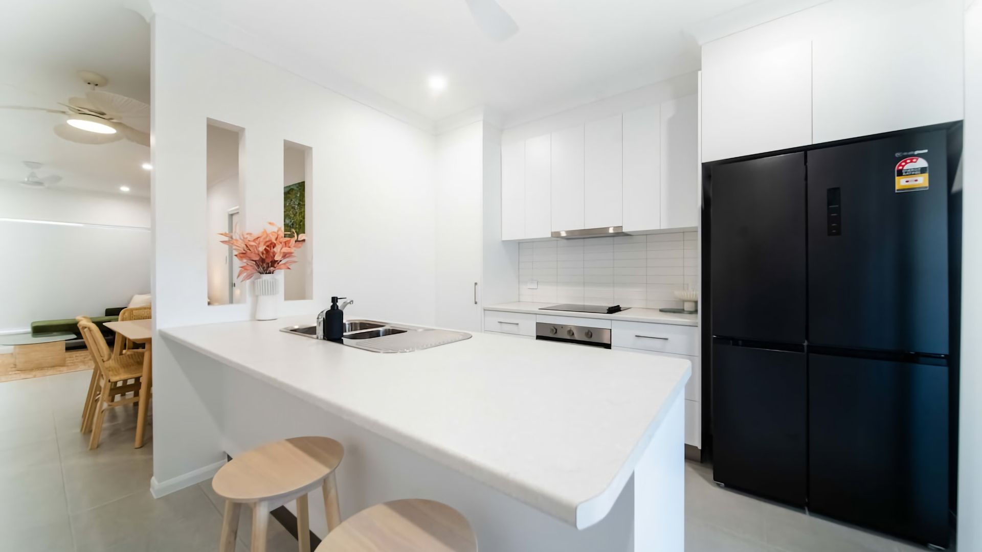 Cozinha moderna com armários brancos, geladeira preta e pequena área de jantar com mesa e cadeiras.