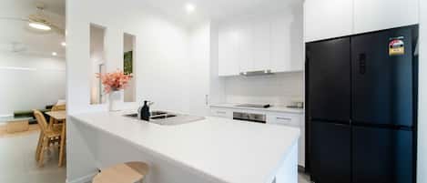 Cozinha moderna com armários brancos, geladeira preta e pequena área de jantar com mesa e cadeiras.