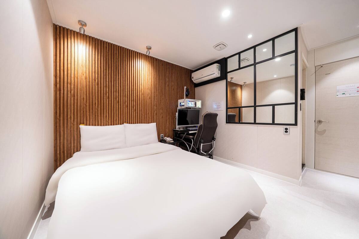 Camera d'albergo con un letto, una scrivania con un computer, un condizionatore d'aria e uno specchio.