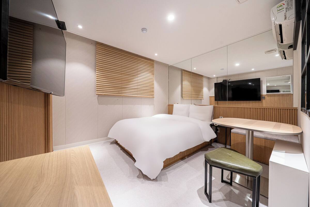 Una camera d'albergo moderna con un letto grande, un tavolino, una panca, una TV e uno specchio.