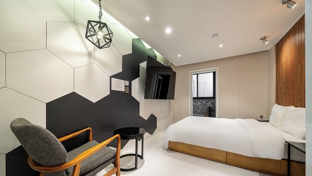 Een moderne slaapkamer met een bed, een stoel, een klein tafeltje en een geometrisch wandontwerp.