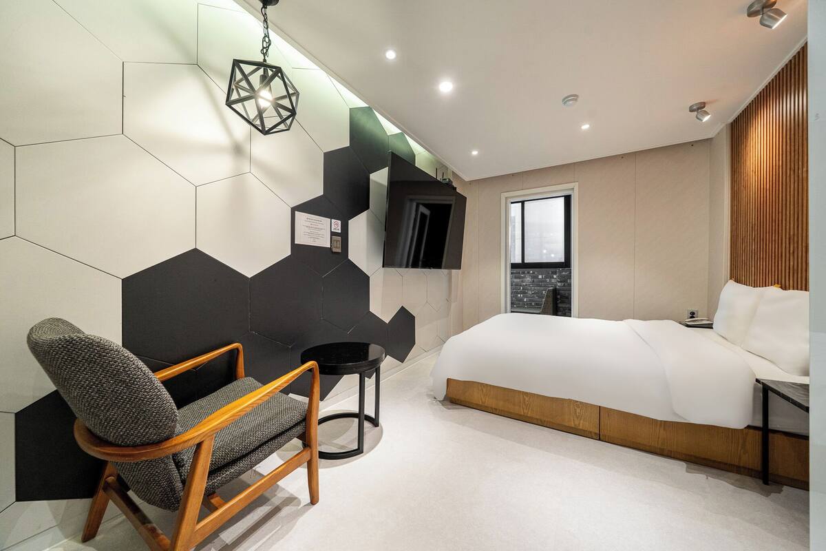 Una camera da letto moderna con un letto, una sedia, un tavolino e un motivo geometrico sulla parete.
