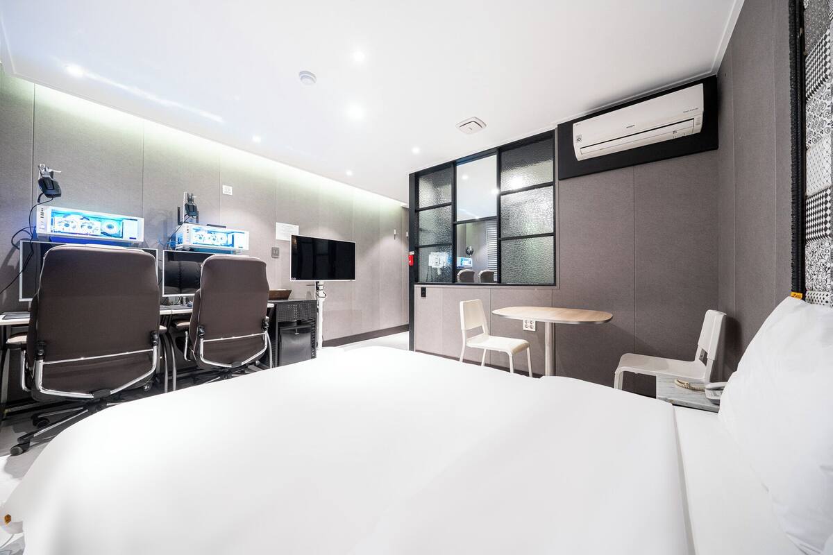 Una camera d'hotel moderna con un letto grande, una scrivania con computer, un tavolino e una sedia.