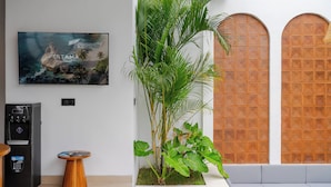 Un intérieur moderne agrémenté d’un distributeur d’eau, d’une petite table en bois, d’une grande plante en pot et d’une œuvre d’art encadrée au mur.
