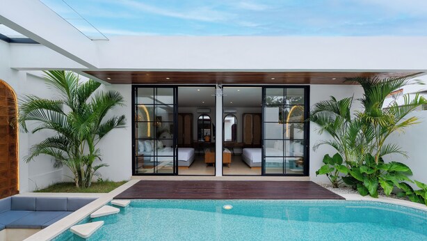 Une maison moderne dotée d’une piscine, de grandes portes vitrées donnant sur un espace de vie et agrémentée de plantes tropicales.