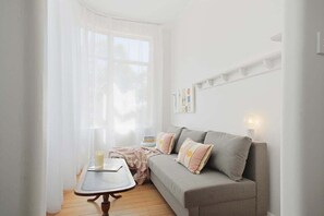 Un salon chaleureux avec un canapé gris, une petite table et une fenêtre ornée de rideaux légers.