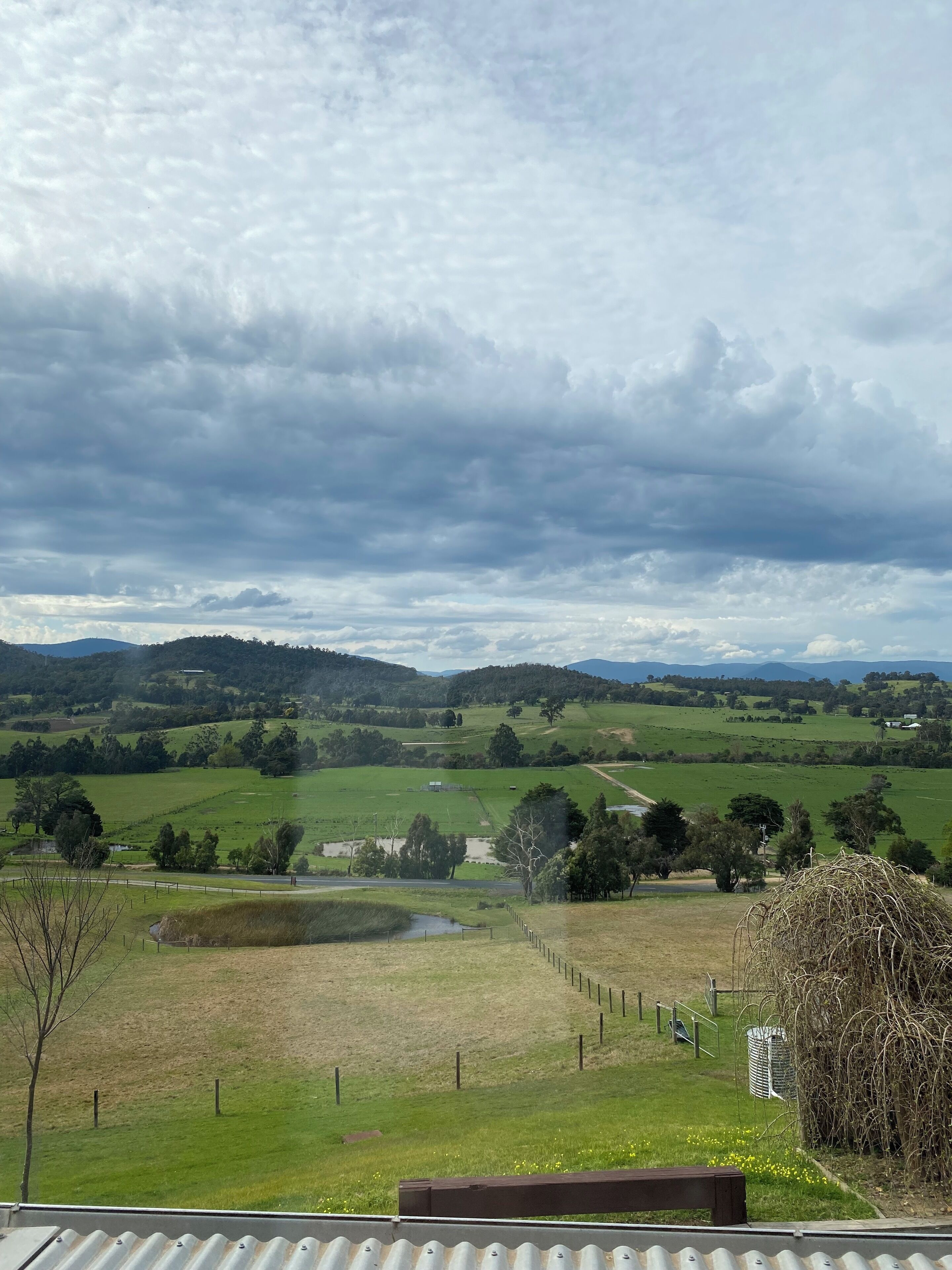 Un paysage rural avec des collines douces, un champ délimité par une clôture et une maison située au loin.