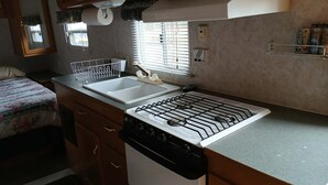 Een kleine keuken met een spoelbak, kookplaat en opslagplanken.