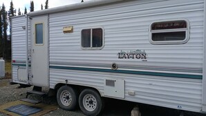 Een stilstaande camper met een schuifdeur, een klein raam en 'LAYTON' branding op de zijkant.