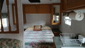 Een slaapkamer met een bed, nachtkastje, spiegel, raam en een klein tafeltje met een mandje.