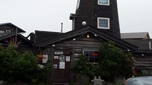 Een blokhutachtige constructie met een opvallende toren, een houten deur met een 'OPEN' bord en een klein raam met een neon 'OPEN' bord.