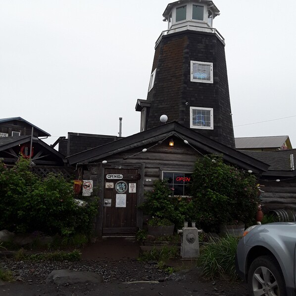 A log cabin-style building with a prominent tower, a wooden door with an 'OPEN' sign, and a small window with a neon 'OPEN' sign.