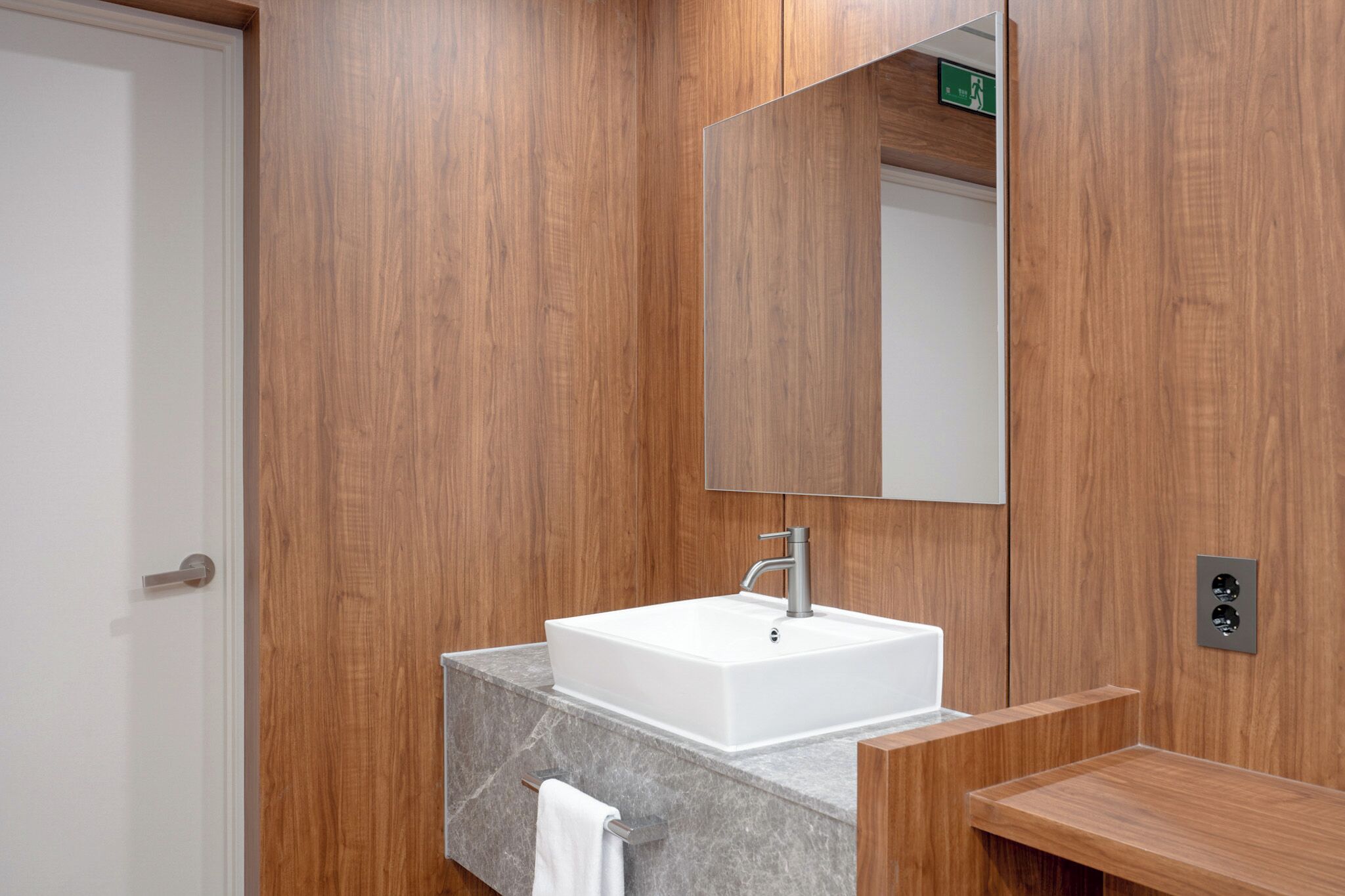 A modern bathroom with a wooden wall, a white sink, a mirror, and a towel rack.
