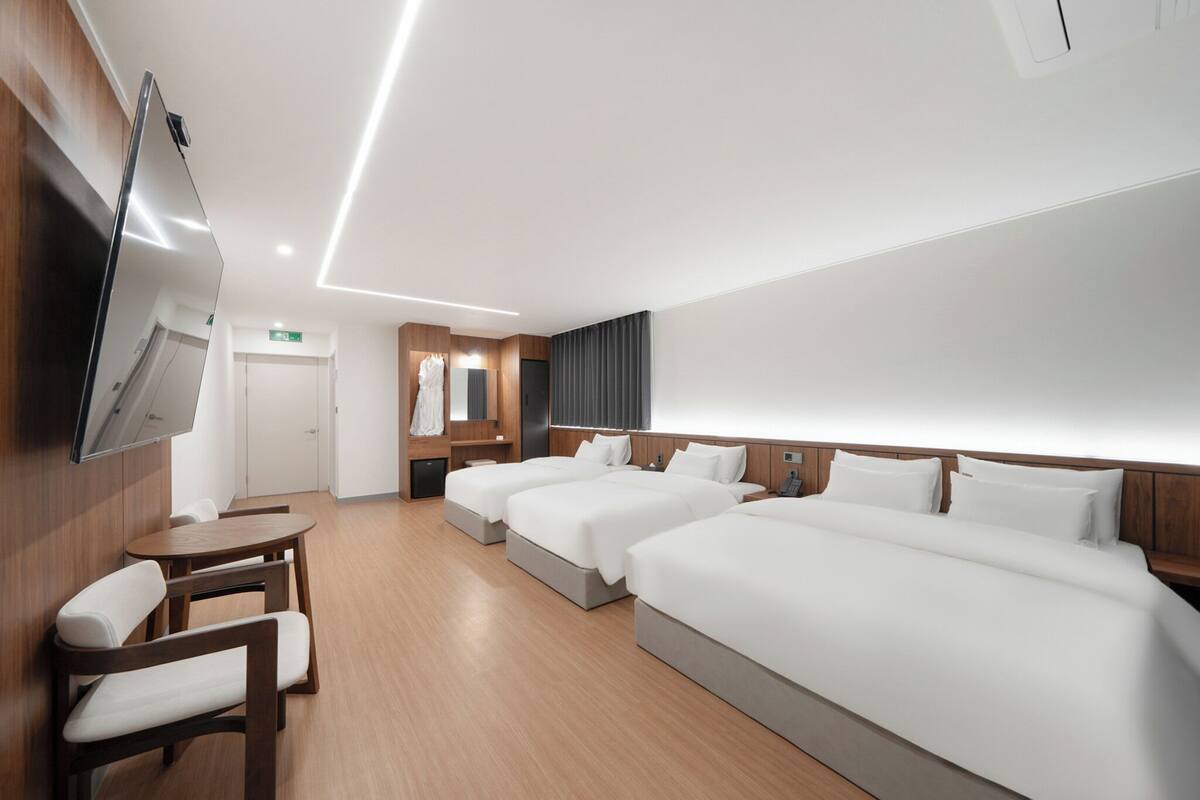 A hotel room with three beds, a TV mounted on the wall, a wooden desk, and a chair.