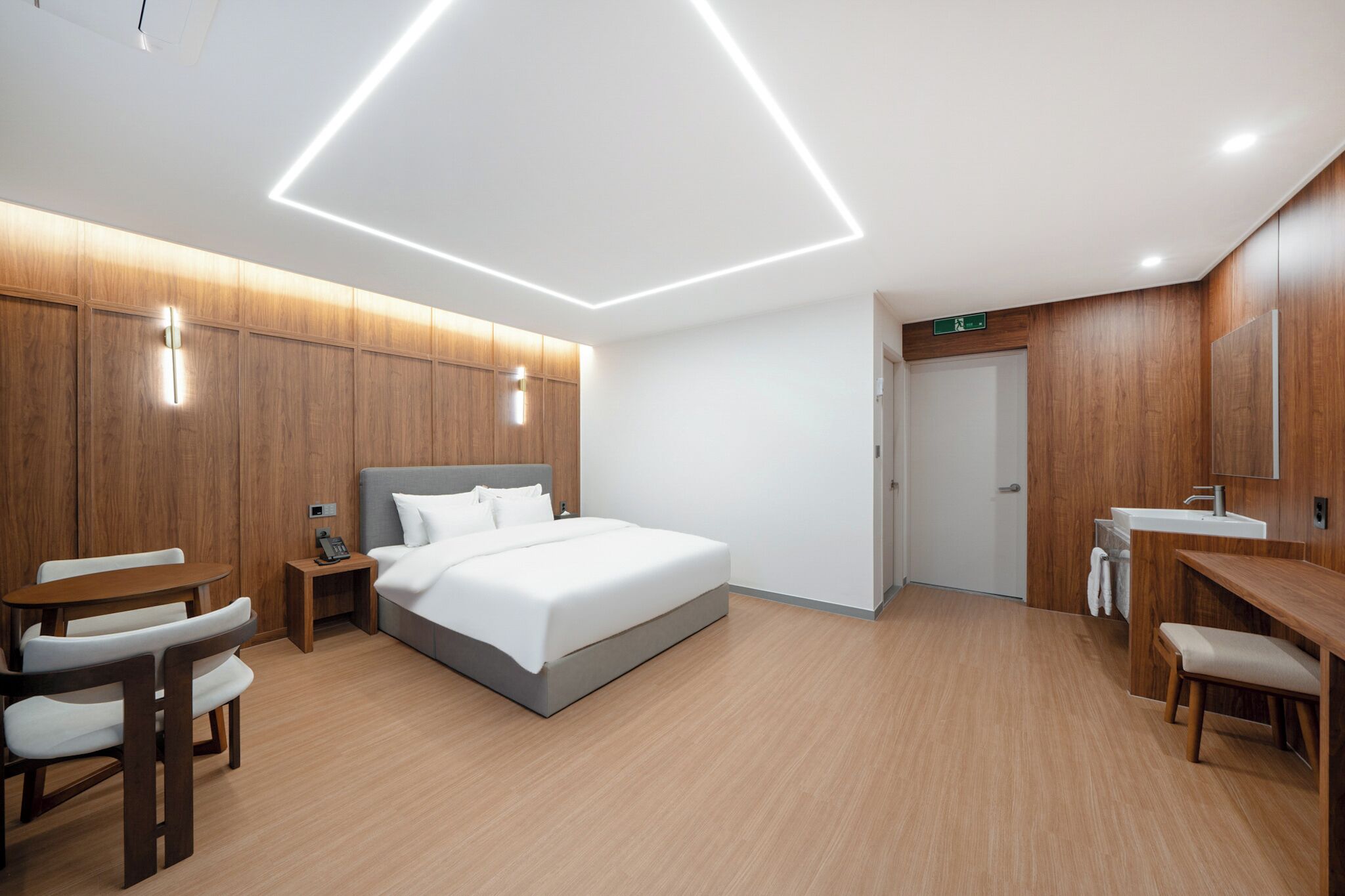 A modern hotel room with a bed, bedside table, chair, and a desk with a chair.