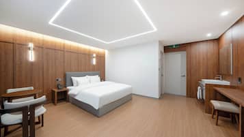 A modern hotel room with a bed, bedside table, chair, and a desk with a chair.