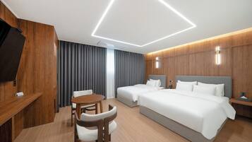 A modern hotel room with a wooden accent wall, a flat-screen TV, a desk, a round table, two beds, and a large window with curtains.