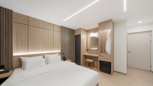 Ein modernes Hotelzimmer mit einem großen Bett, einem eingebauten Kleiderschrank, einem Nachttisch und einem kleinen Schreibtisch mit Stuhl.