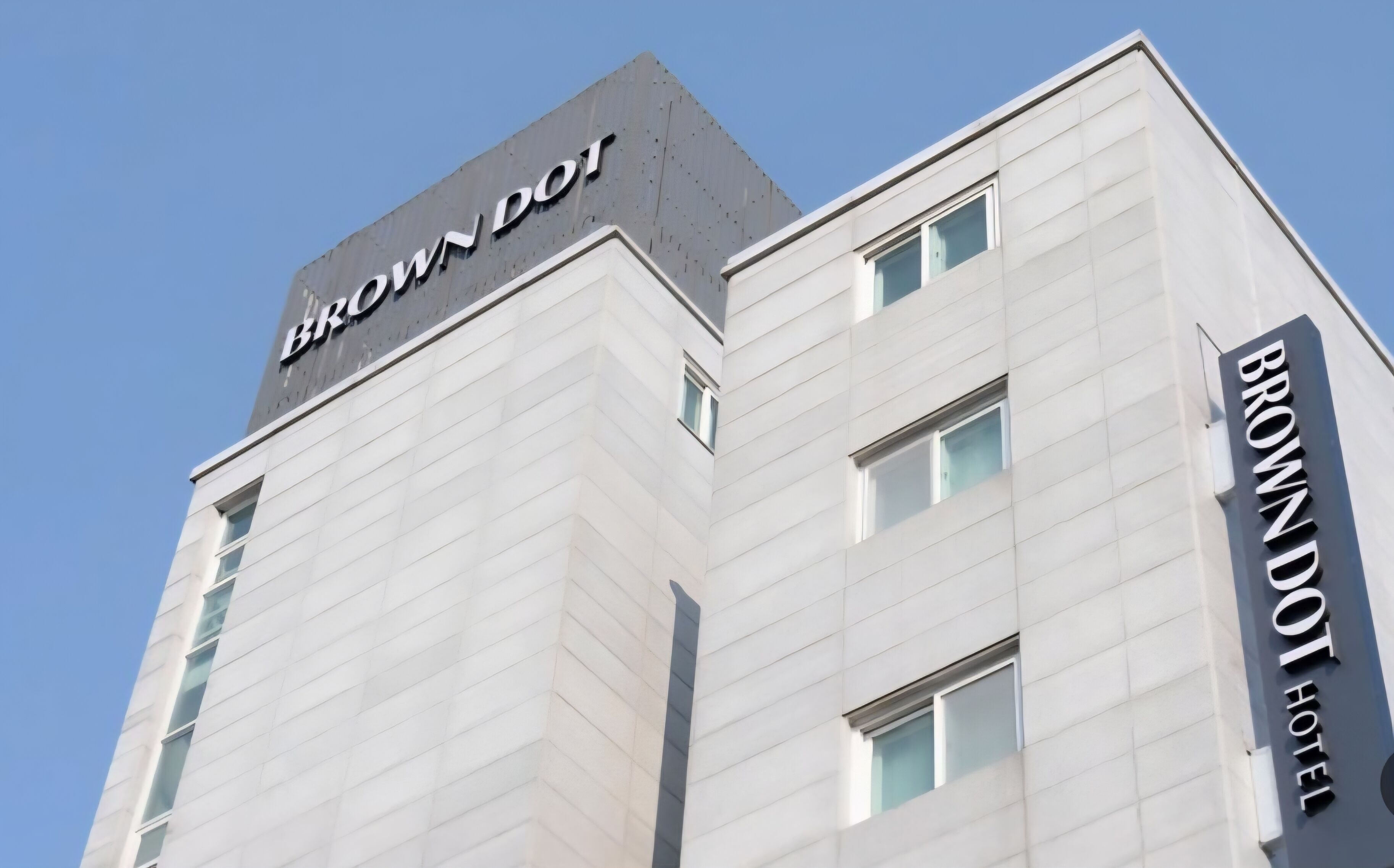 Ein modernes Hotelgebäude mit einem gut sichtbaren 'BROWN DOT HOTEL'-Schild an der Fassade.
