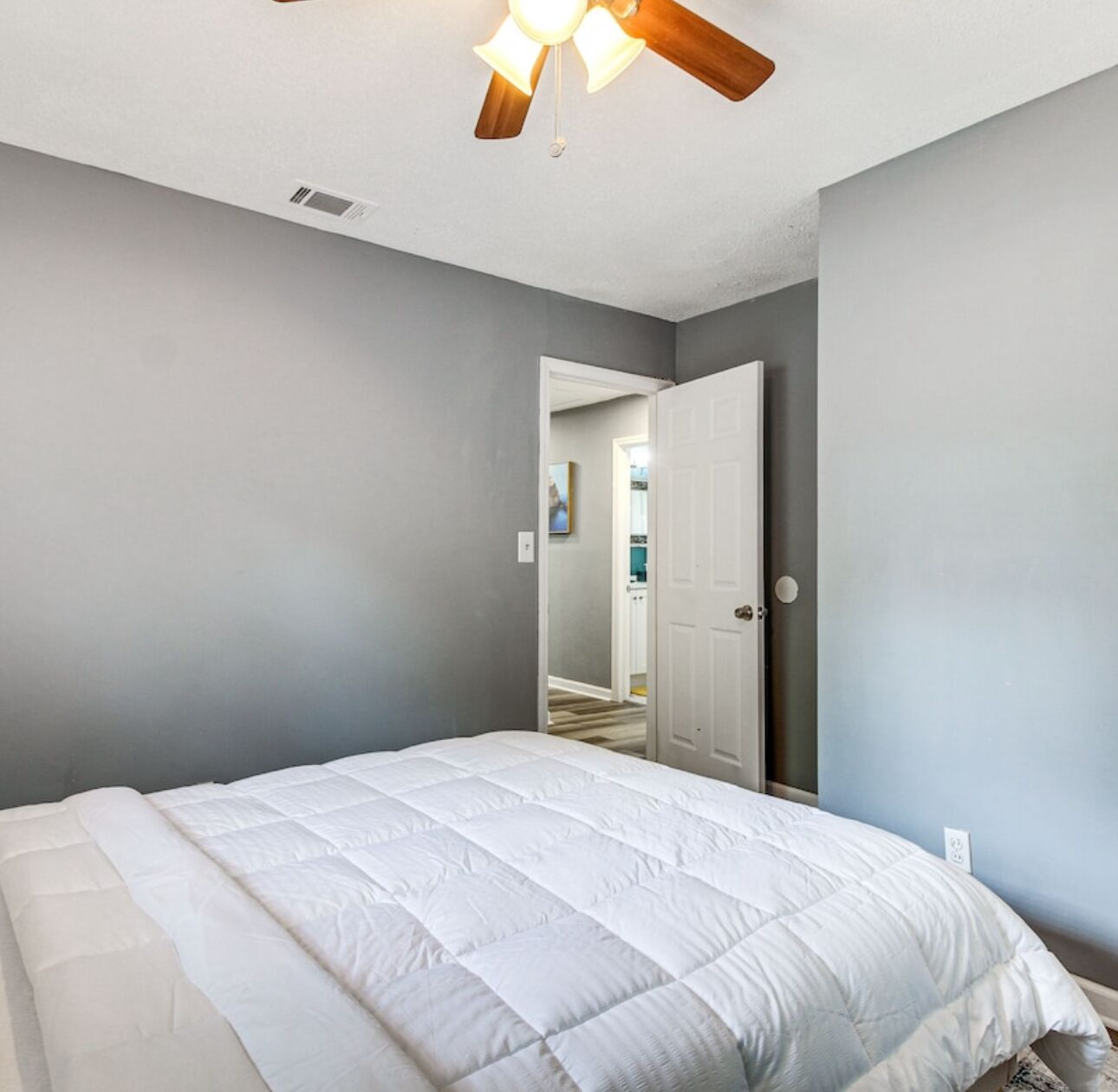 A bedroom with a large bed, a ceiling fan, and a door leading to another room.