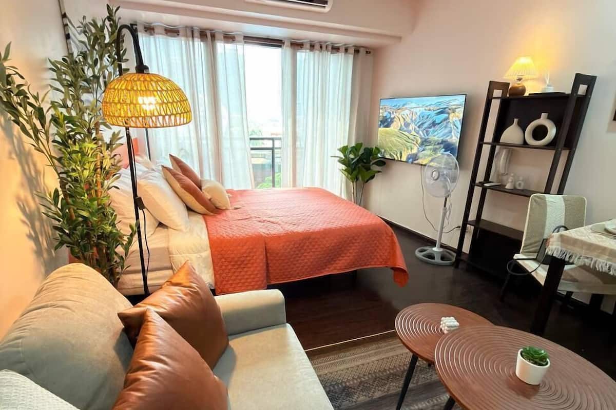 Een hotelkamer met een bed, een sofa, nachtkastje, airconditioning en een schilderij aan de muur.