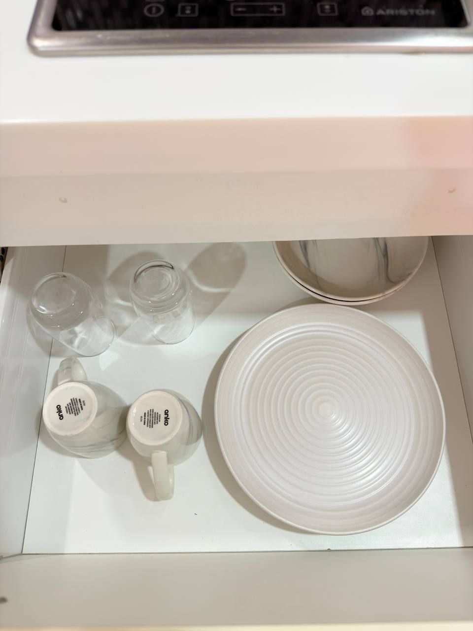 A kitchen drawer with various glassware and a white plate.