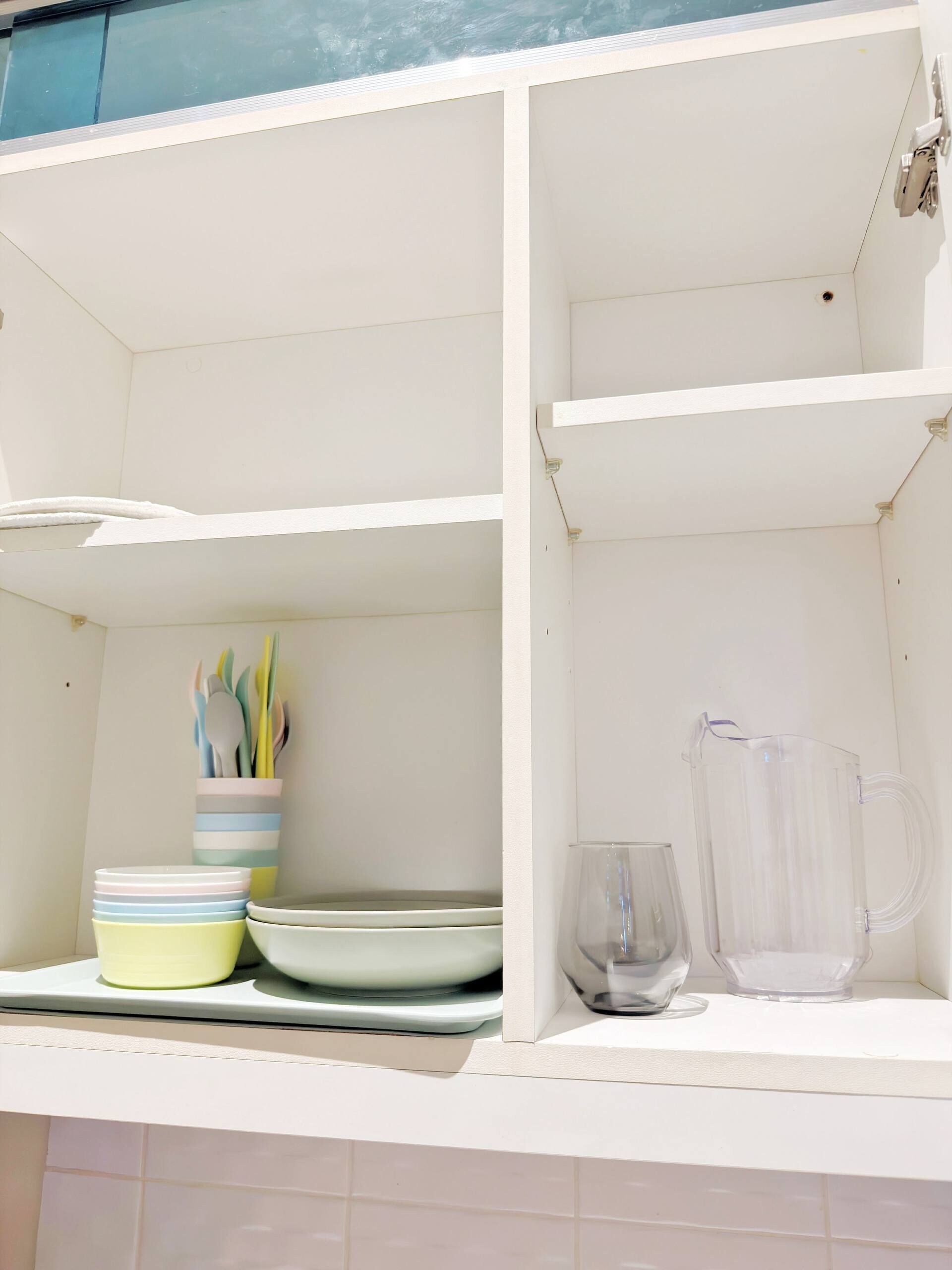 A kitchen with white cabinets, a clear glass pitcher, and a stack of plates.