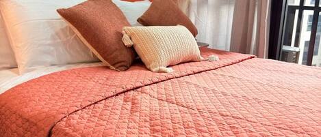 A bed with a pink quilt, white and brown pillows, and a wooden headboard.