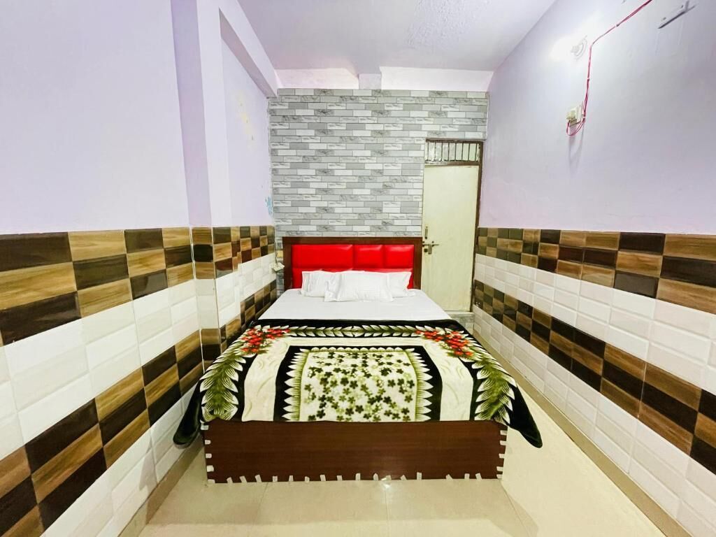A narrow hotel room with a bed, a red headboard, and a patterned floor.
