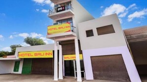 Un hôtel moderne, reconnaissable à son grand panneau « HOTEL BALI INN », doté d’un balcon à l’étage supérieur et d’une entrée sécurisée par un portail.