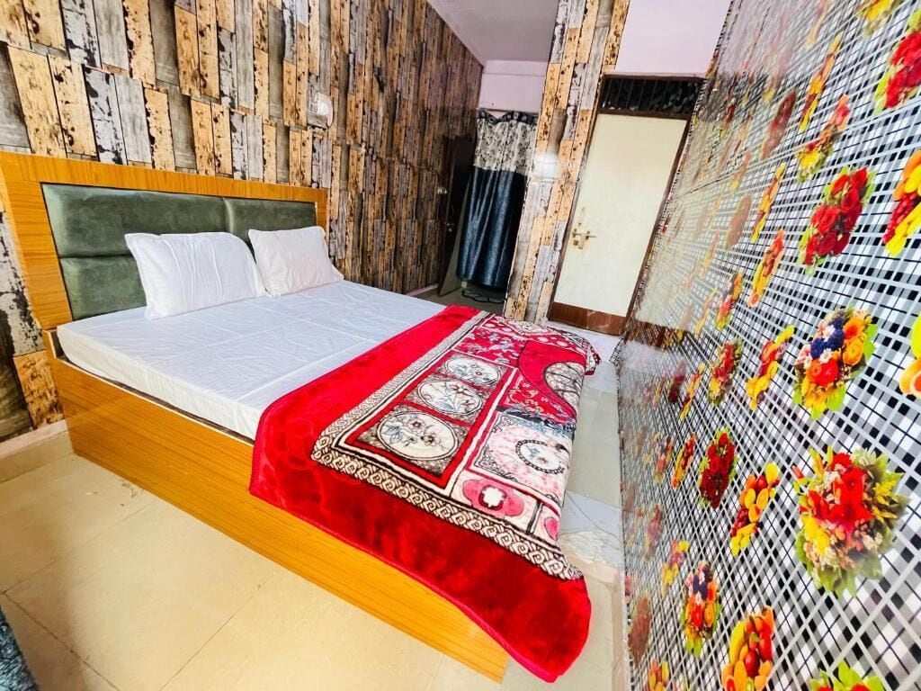 Une chambre à coucher avec une tête de lit en bois, un lit recouvert d’une courtepointe à motifs rouges et blancs, et un mur décoratif agrémenté de compositions florales.