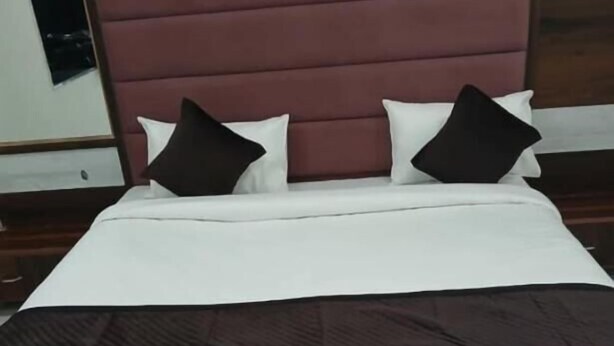 Un lit bien fait, avec une literie blanche et marron, une tête de lit en bois et deux oreillers noirs.