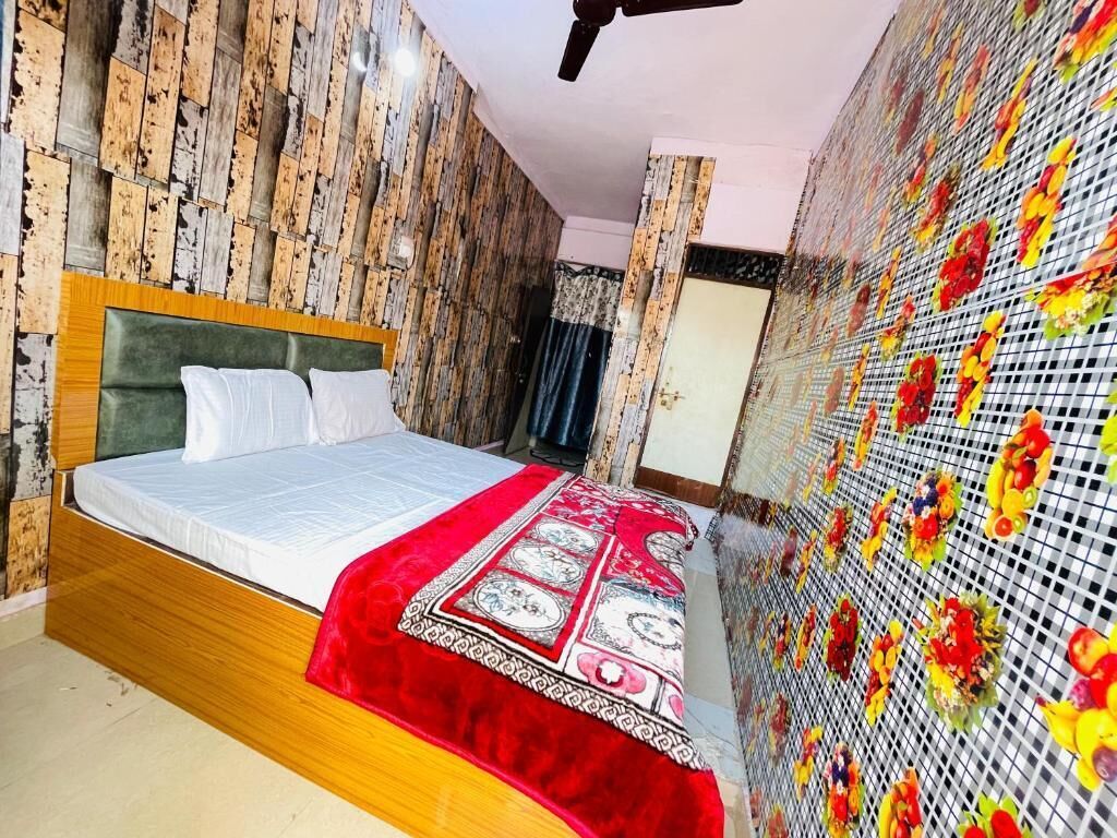 A bedroom with a wooden bed frame, a red and white patterned bedspread, and a wall decorated with a floral grid pattern.