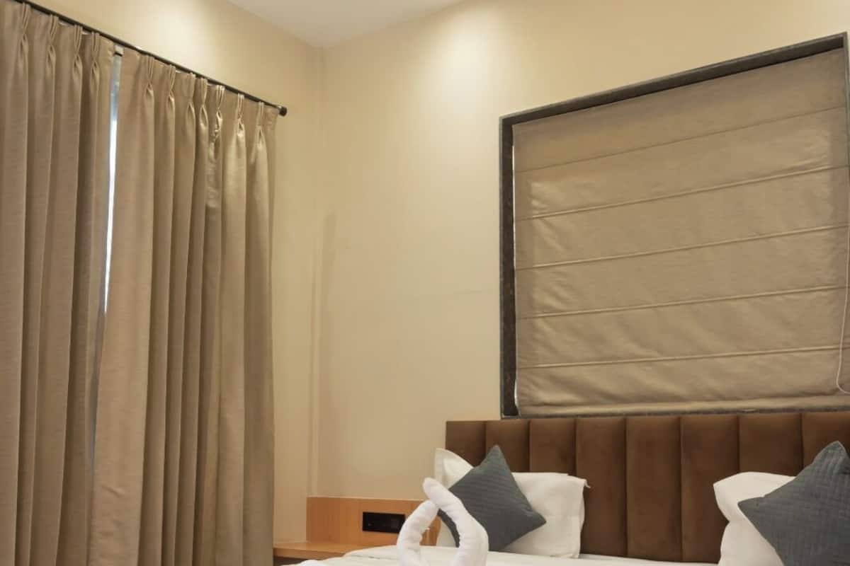 A modern hotel room with a large bed, beige curtains, a ceiling fan, and a blue rug.