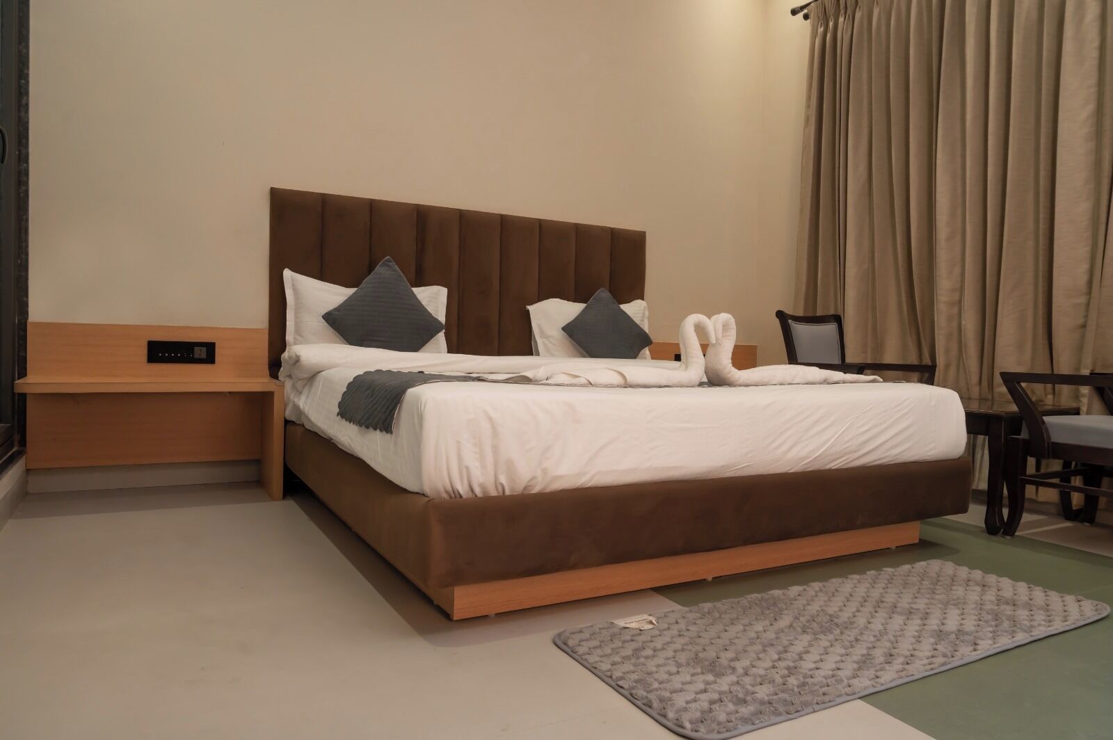 Een keurig opgemaakt bed met een bruin hoofdbord, een nachtkastje en een stoel.
