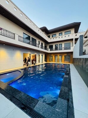 A modern building with a central swimming pool, multiple balconies, and a mix of indoor and outdoor spaces. - Sukuun (Amritsar)