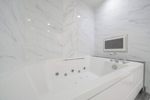 Ein modernes Badezimmer mit einer großen, weißen Badewanne, einem integrierten Fernseher und Marmorwänden.