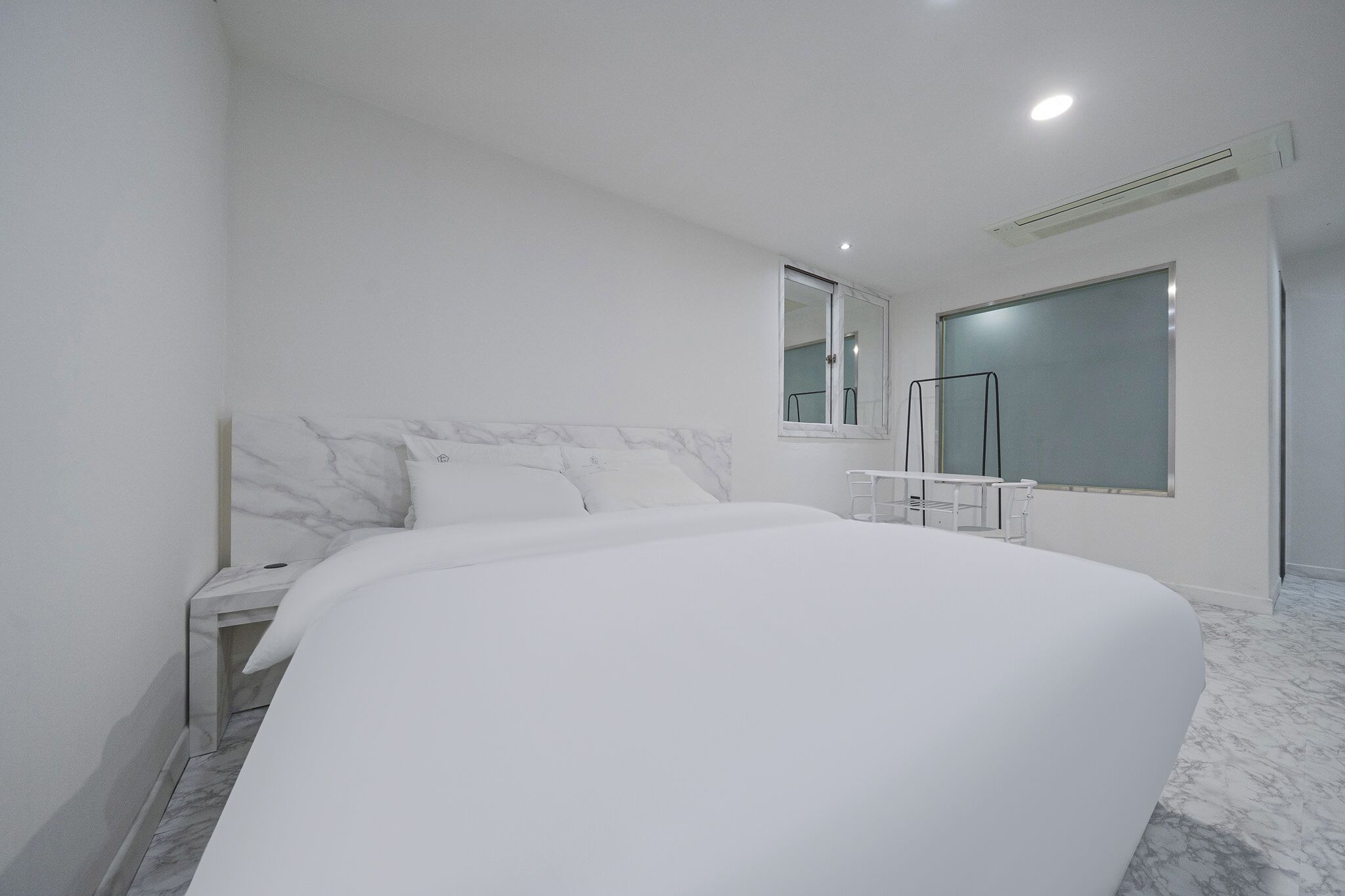 A modern bedroom with a large bed, a bedside table, a mirror, and a window.