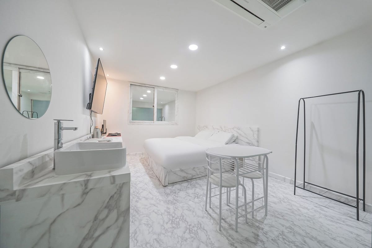 Een moderne badkamer met een marmeren wastafel, een grote spiegel, een bed, een klein tafeltje en een douchehoek.