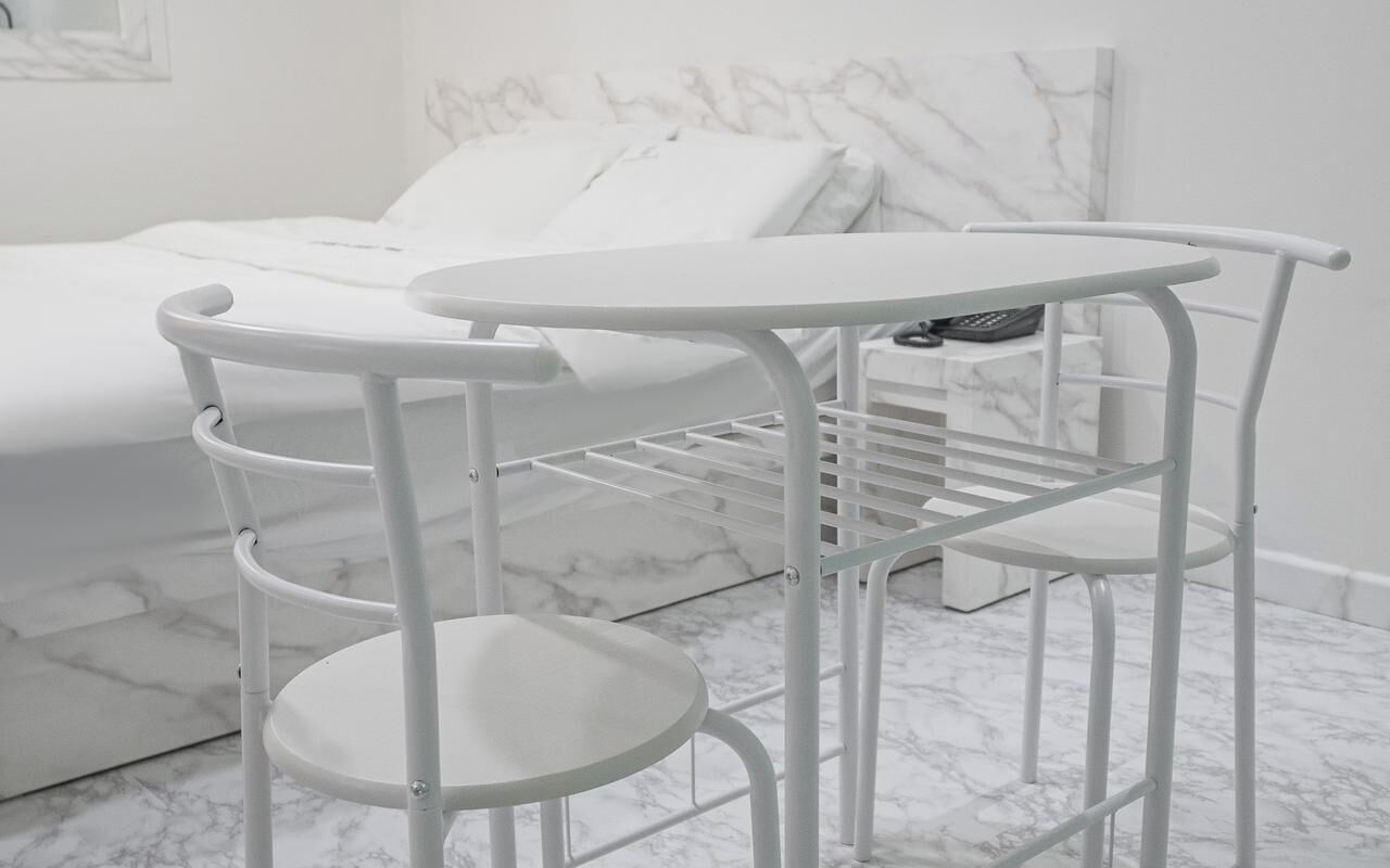 A white metal chair with a small table, a white bed, and a marble floor.