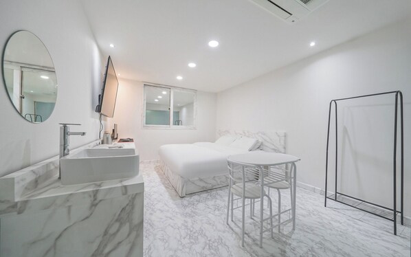 Ein modernes Schlafzimmer mit Marmorbad, einem Bett, einem kleinen Tisch und einer Duschkabine.