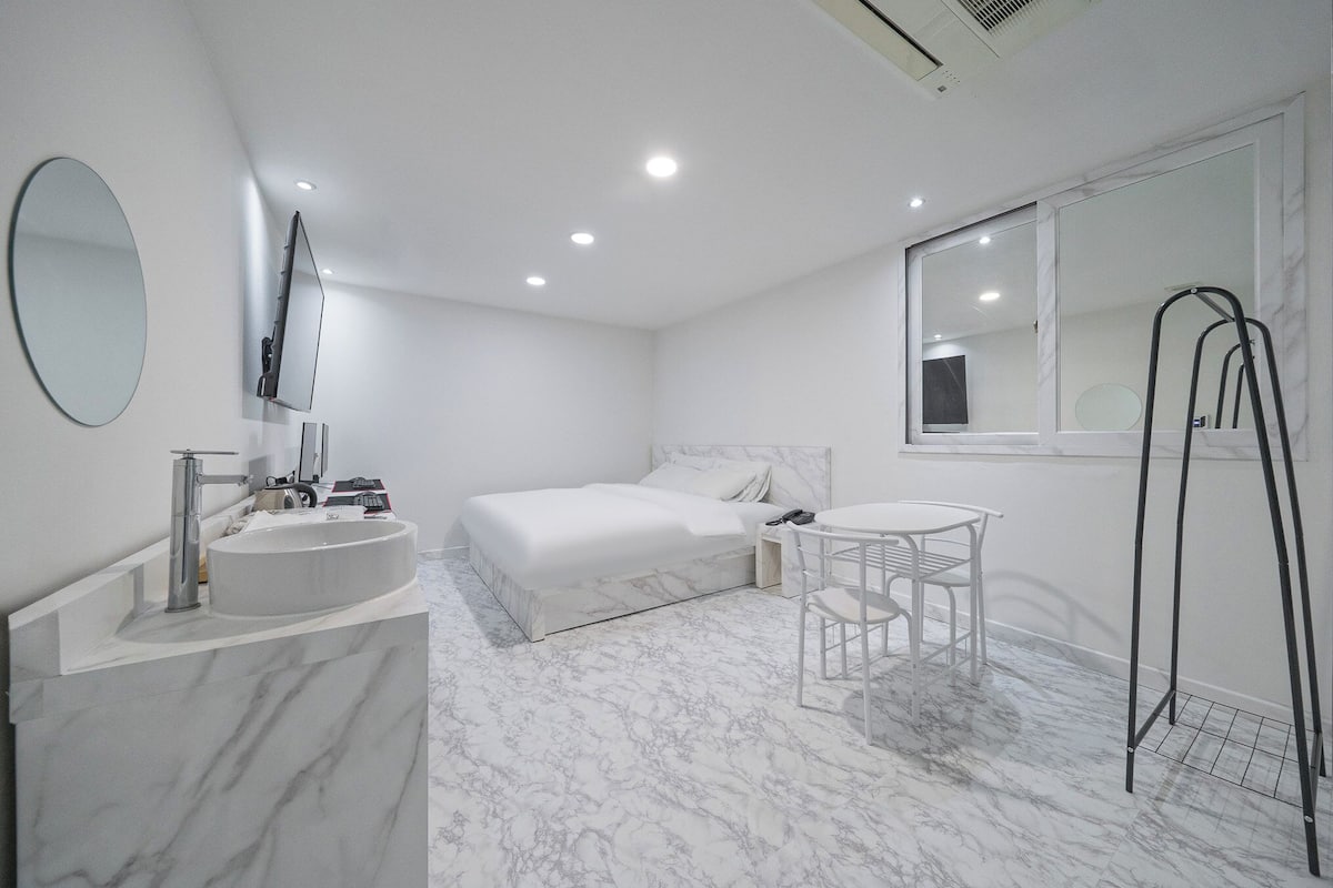 Een moderne badkamer met een marmeren wastafel, een grote spiegel, een bed en een kleine tafel met stoelen.