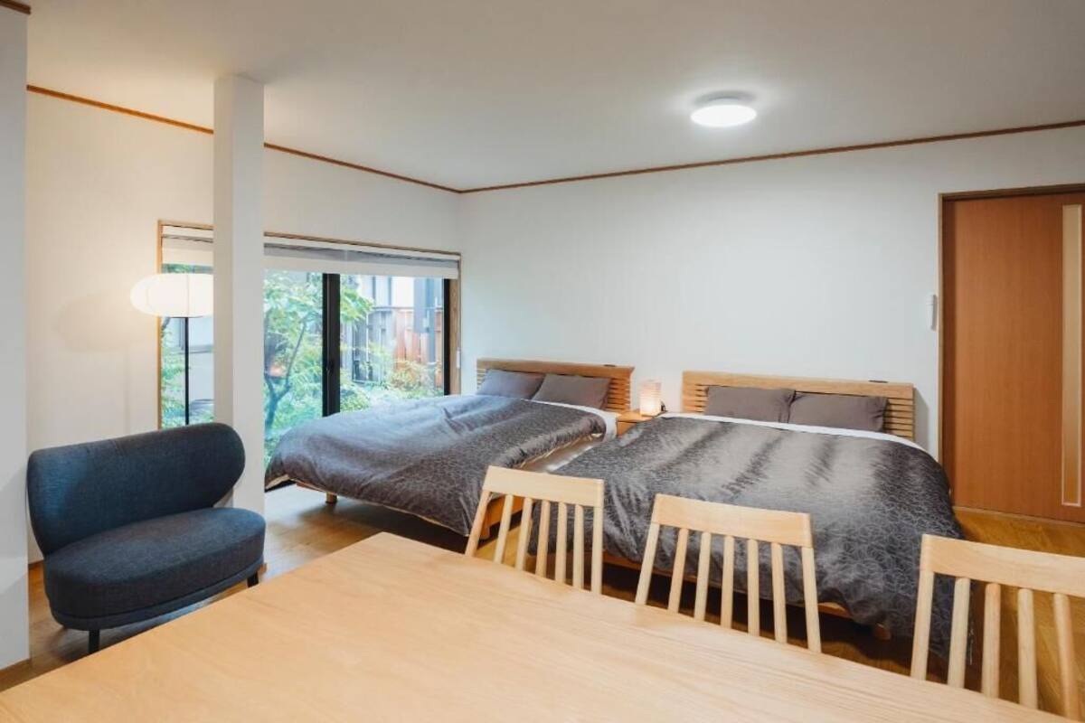 A bedroom with two beds, a table, and a chair.