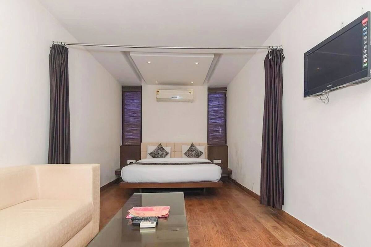 A hotel room with a bed, a sofa, a TV, and an air conditioning unit.