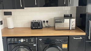 Eine kleine Küche mit schwarzen Schränken, einem Toaster, einem Reiskocher und zwei Waschmaschinen mit Frontlader.