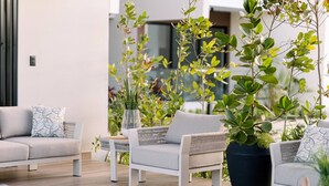 A modern living room with a grey sofa, a white armchair, and a coffee table. There are potted plants and a small table with decorative items. - Mountain and Pool Modern Apartment (Santiago de los Caballeros)